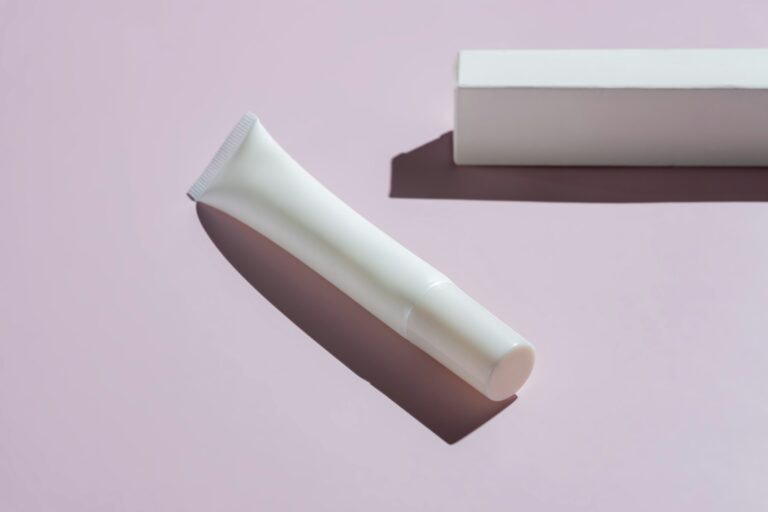 Eye cream package mockup. Unbranded plastic tube and paper box on pink background with harsh shadows